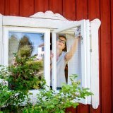 Kvinna som tvättar fönstren i faluröd stuga